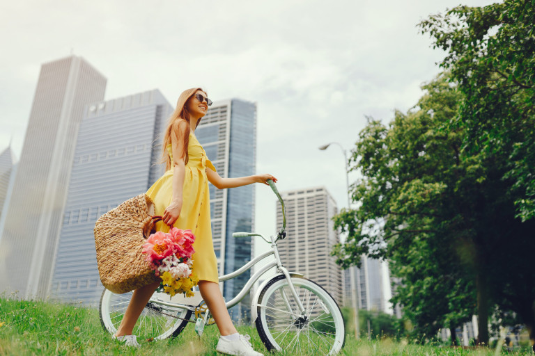 a cute and stylish girl in a yellow dress and long hair rides on a bicycle with a basket of flowers in the sunny summer city pretty girl with bicycle